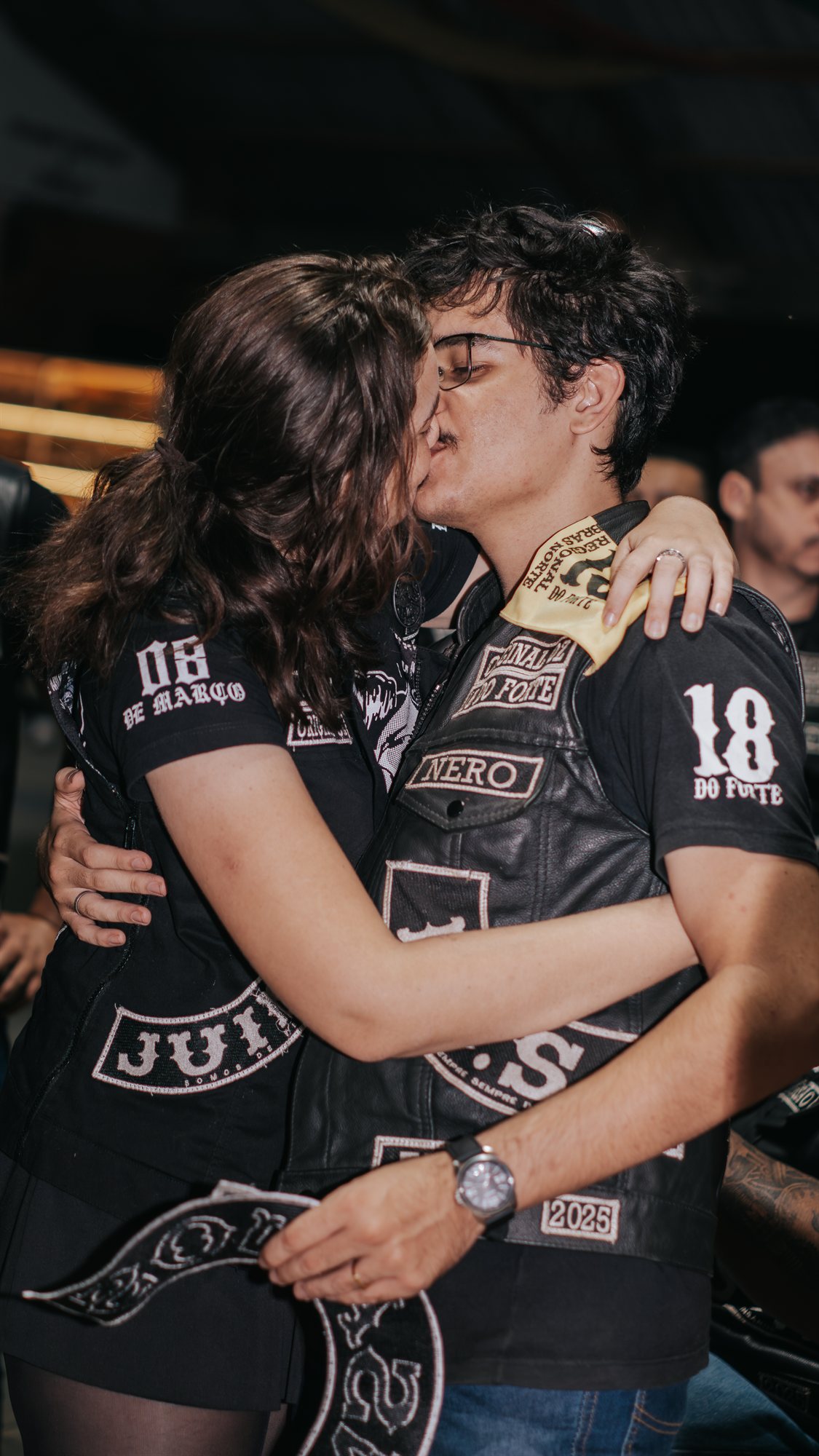 Casal se beijando vestindo jaquetas de motoclube